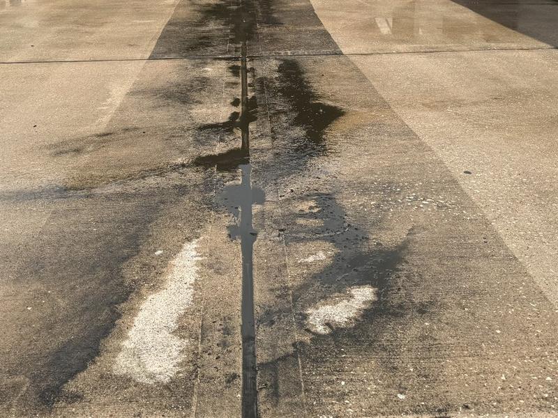 Close view of a driveway partway through cleaning: lighter concrete on both sides of a darker strip